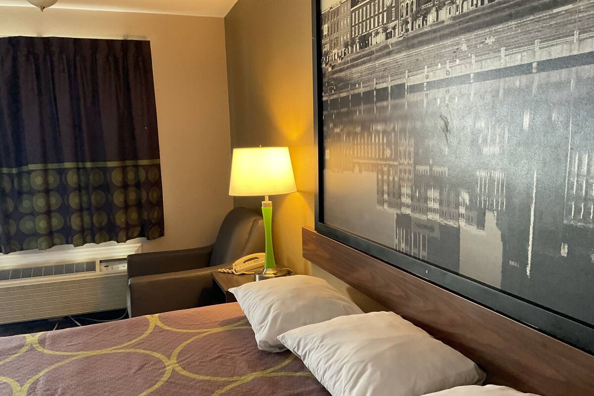 A hotel room with a bed, a desk, a lamp, a telephone, and a large framed picture on the wall.