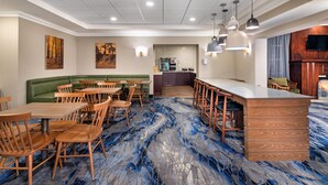 A spacious dining area with wooden tables and chairs, a green sofa, and a kitchen in the background. - Fairfield Inn by Marriott Toronto Oakville (Oakville)