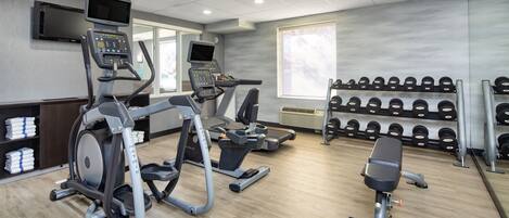 A gym with treadmills, an elliptical, a bench press, and a rack of dumbbells.