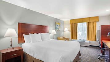A hotel room with a large bed, two bedside tables with lamps, a desk with a chair, a window with curtains, and a painting on the wall.