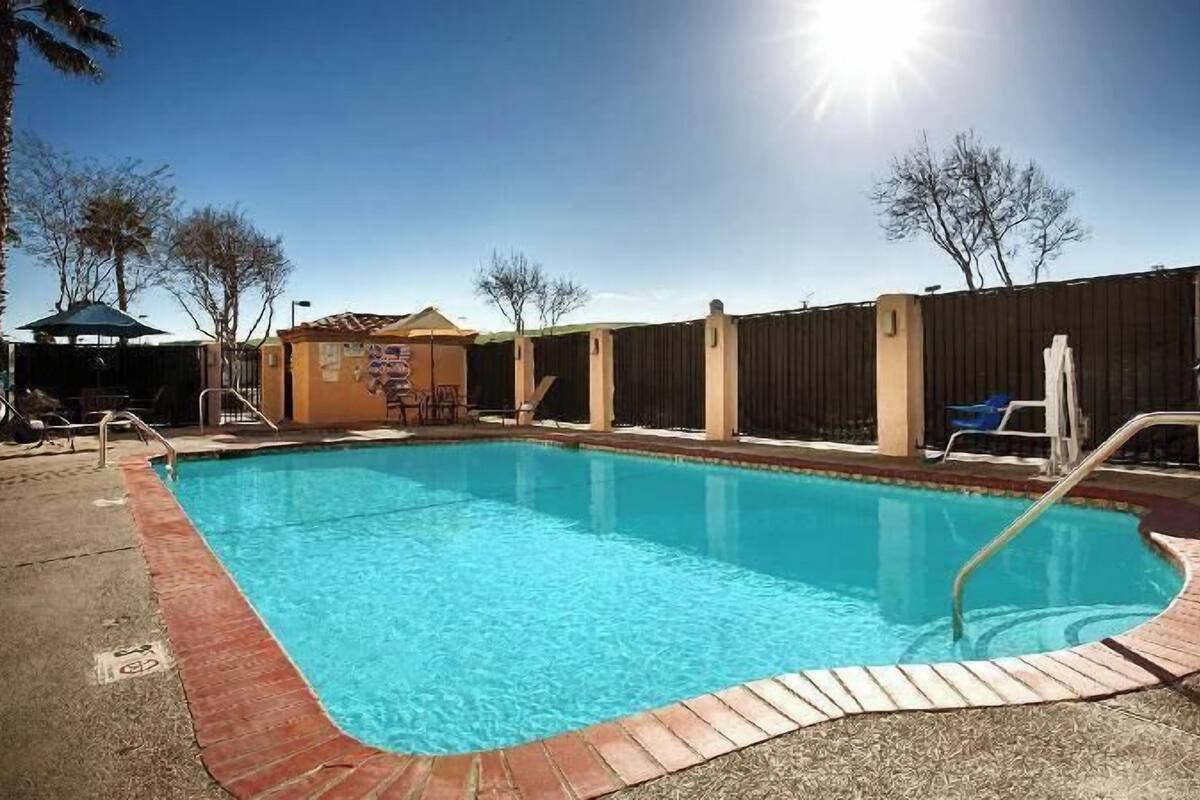 A rectangular swimming pool with a brick edge, surrounded by a fence, and a clear sky above.