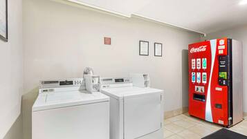 Un espace buanderie avec deux machines à laver blanches et un distributeur automatique de boissons Coca-Cola rouge.