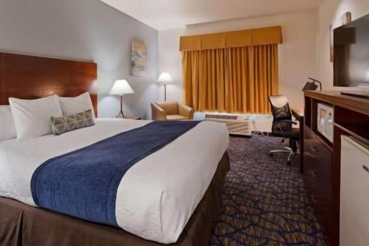A hotel room with a large bed, a desk, a chair, a television, and a window with curtains.