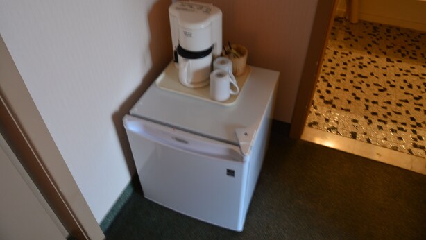 Un petit réfrigérateur, doté d’une machine à café et d’un porte-gobelet, se trouve dans une petite pièce dont le sol est recouvert d’un motif décoratif.