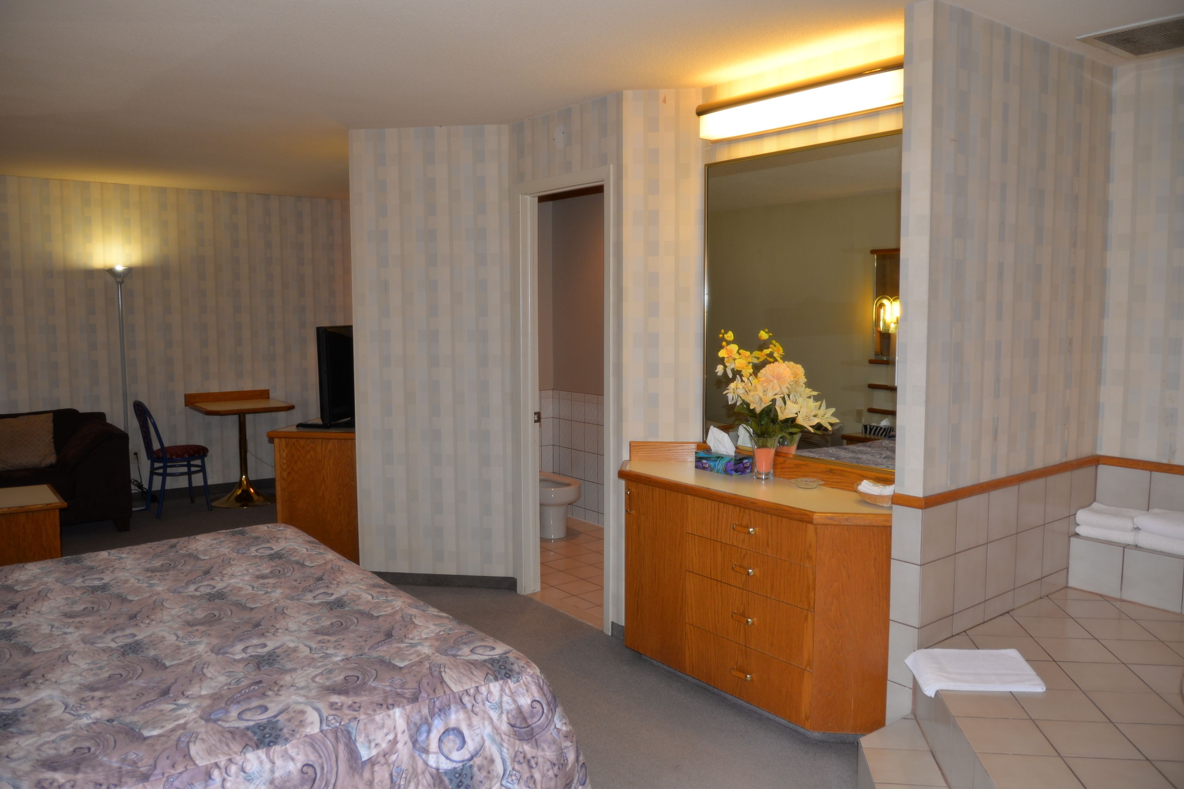 Une chambre d’hôtel comprenant un lit, un bureau, une chaise, une salle de bain avec un lavabo et un miroir, ainsi qu’un espace douche.