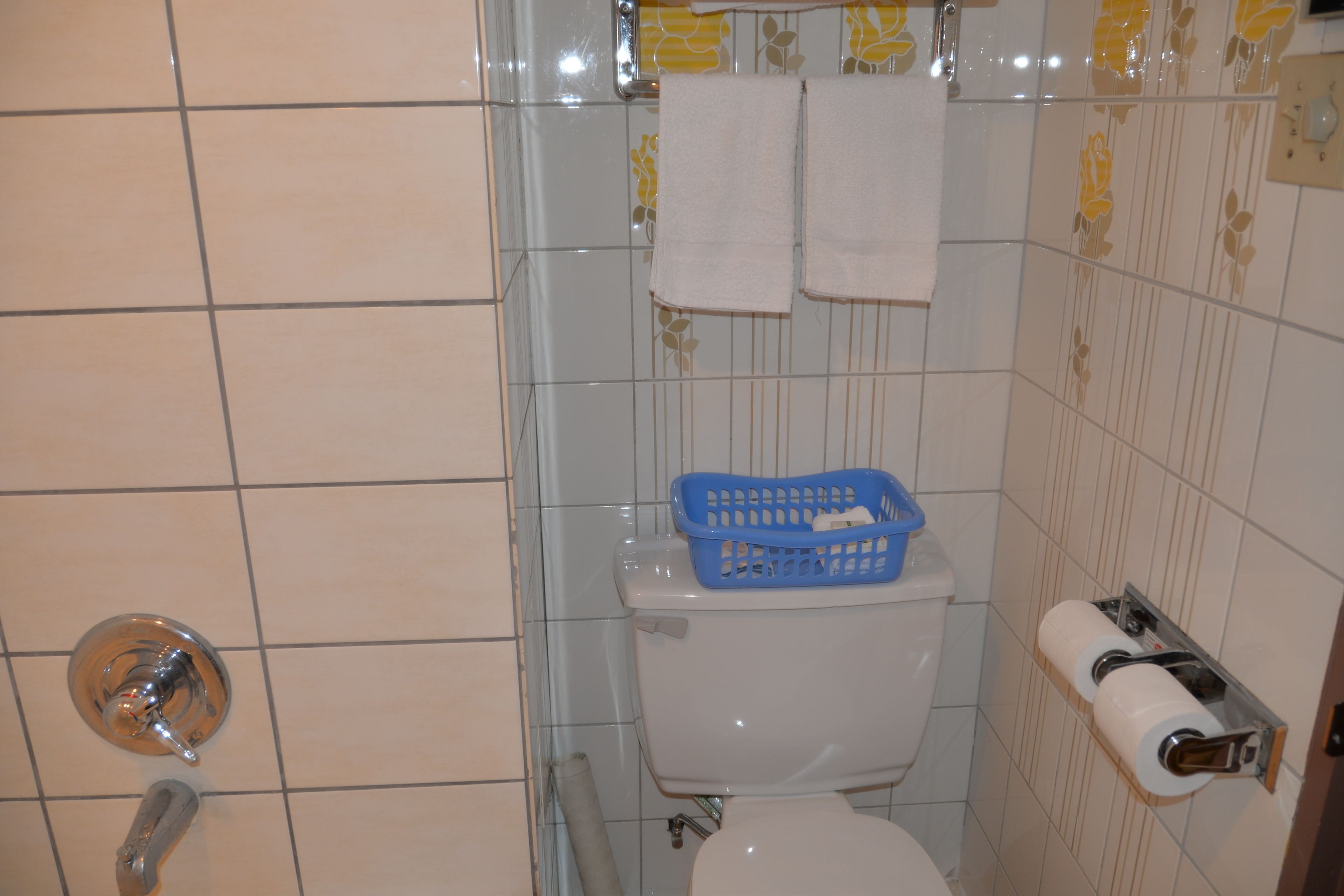 A bathroom with a toilet, a blue basket, and a toilet paper holder.