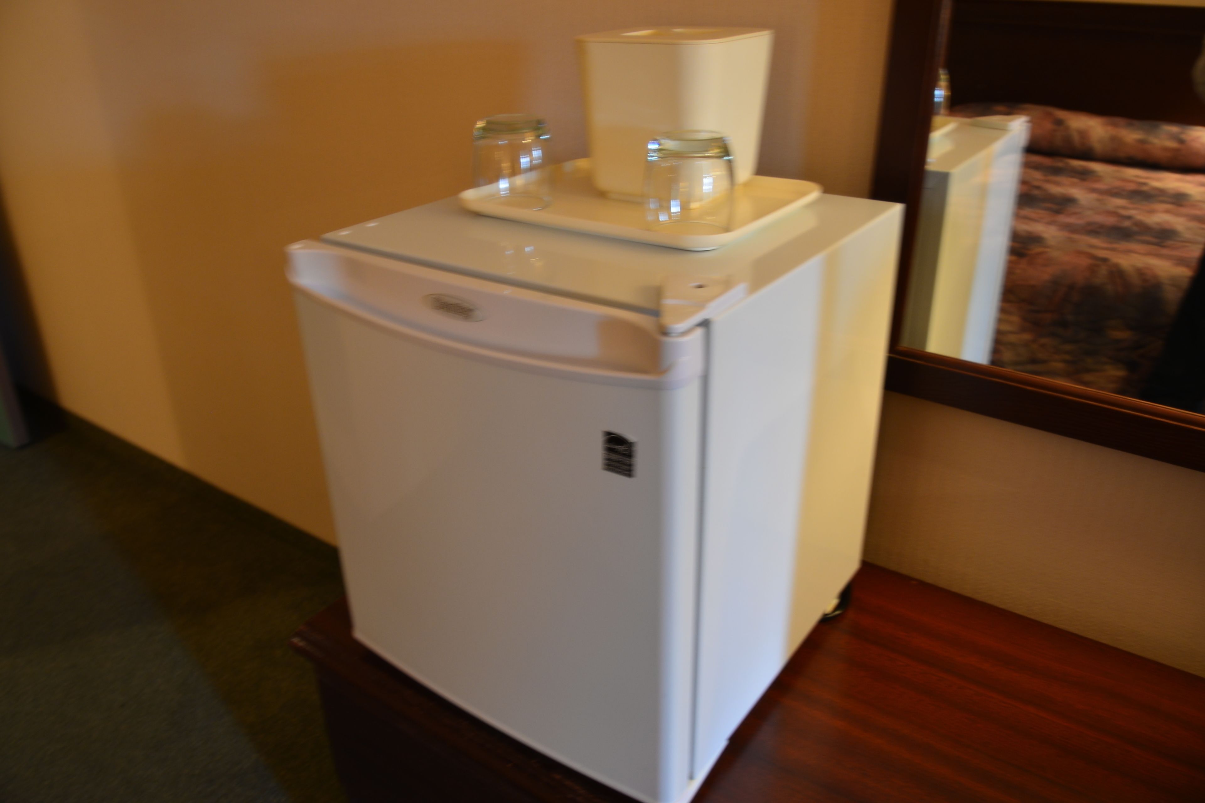Un petit réfrigérateur blanc, doté d’un compartiment congélateur, est posé sur une surface en bois dans une chambre d’hôtel.