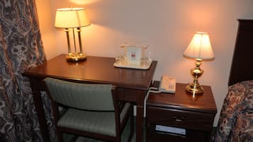 Et hotelværelse med et træskrivebord, to lamper, en telefon og et sengebord med lampe.