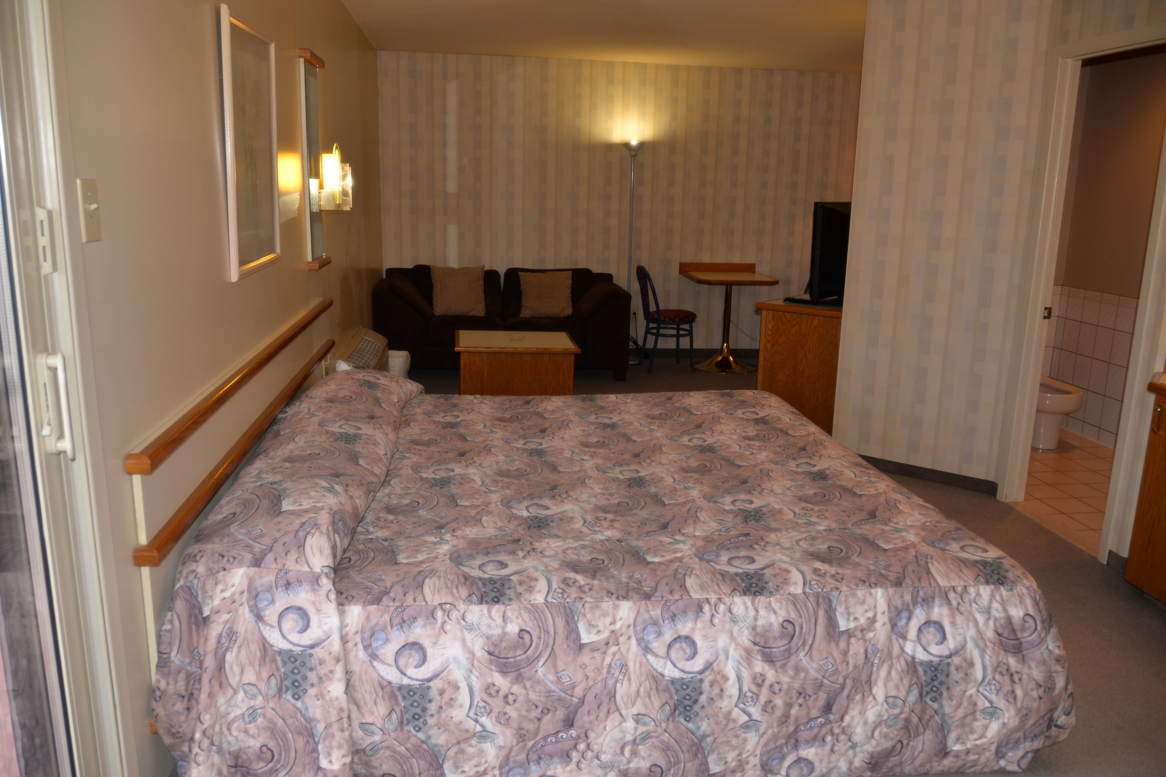 Una habitación de hotel con una cama grande, un sofá, una mesita y un televisor.