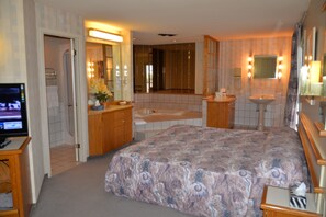 A hotel room with a large bed, a bathroom with a bathtub, a sink, and a mirror. - Travelodge by Wyndham Saint-Liboire (Saint-liboire)