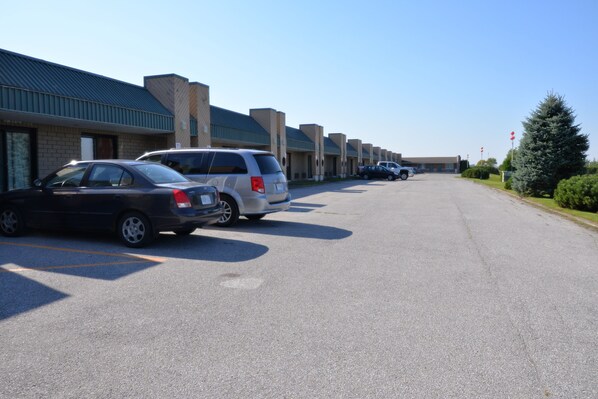A parking lot with several cars parked in front of a row of buildings with a flat roof and brick facade. - Travelodge by Wyndham Saint-Liboire (Saint-liboire)