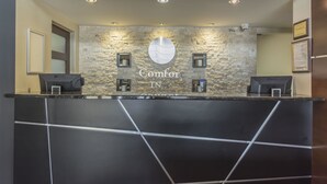 A reception desk with a stone wall background, two computer monitors, and a sign that reads "Comfort in." - Comfort Inn (Saint Georges)