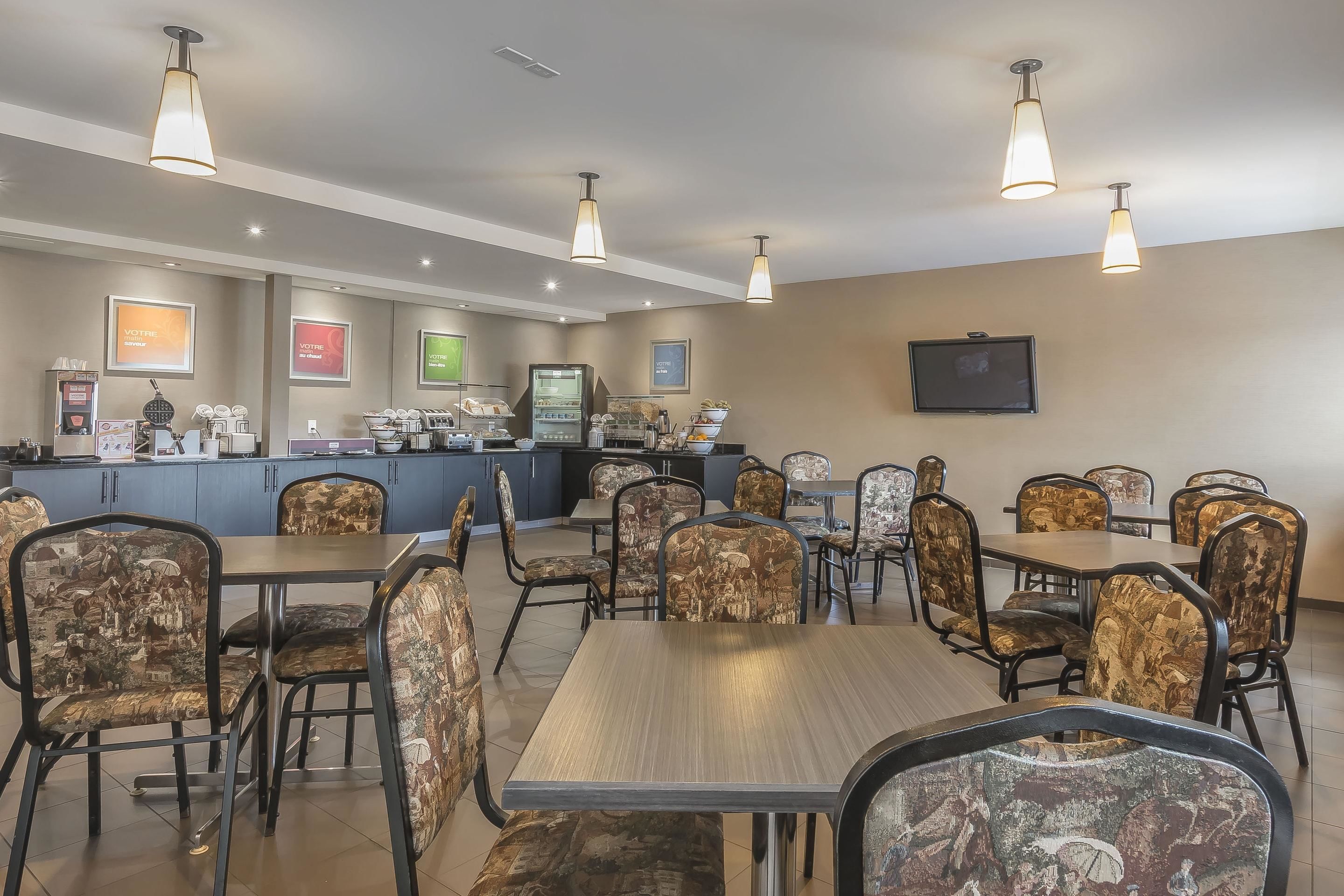 Un restaurante con mesas y sillas, una barra con el menú, y un televisor en la pared.