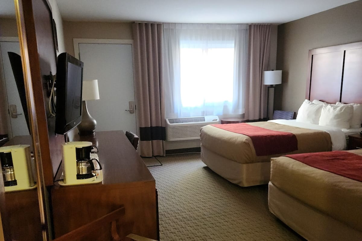 Habitación de hotel con cama, escritorio con computadora y lámpara, una silla, televisor y ventana con cortinas.