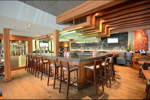 Un espace bar moderne doté d’un îlot central, de tabourets de bar et d’un plafond en bois au design original.