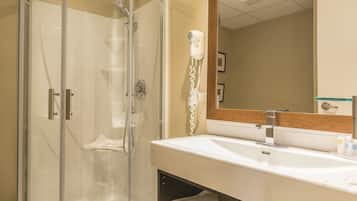 Une salle de bain moderne avec une douche à parois de verre, un lavabo blanc et un sèche-cheveux fixé au mur.
