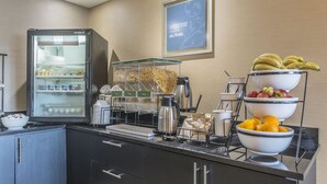 A hotel breakfast area with a refrigerator, coffee maker, and fruit bowls. - Comfort Inn (Saint Georges)