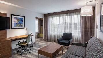 Una habitación de hotel con escritorio, silla de oficina, sofá y un ventanal con cortinas.