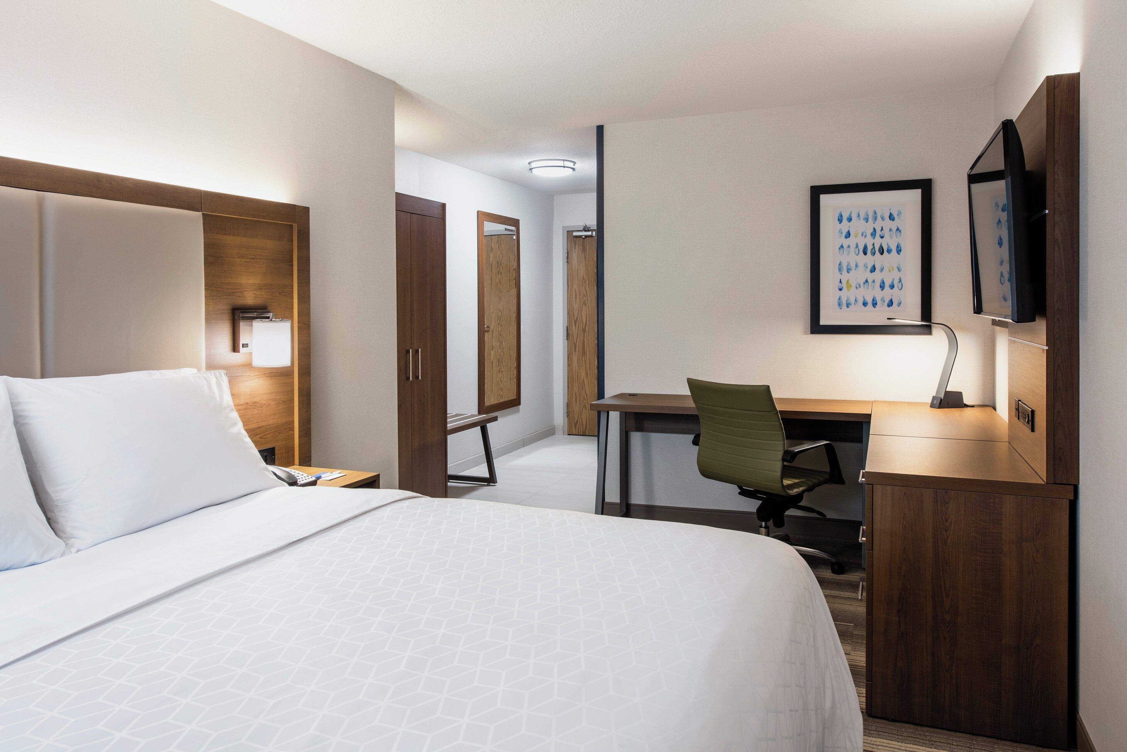 A hotel room with a bed, desk, chair, and a TV on the wall.