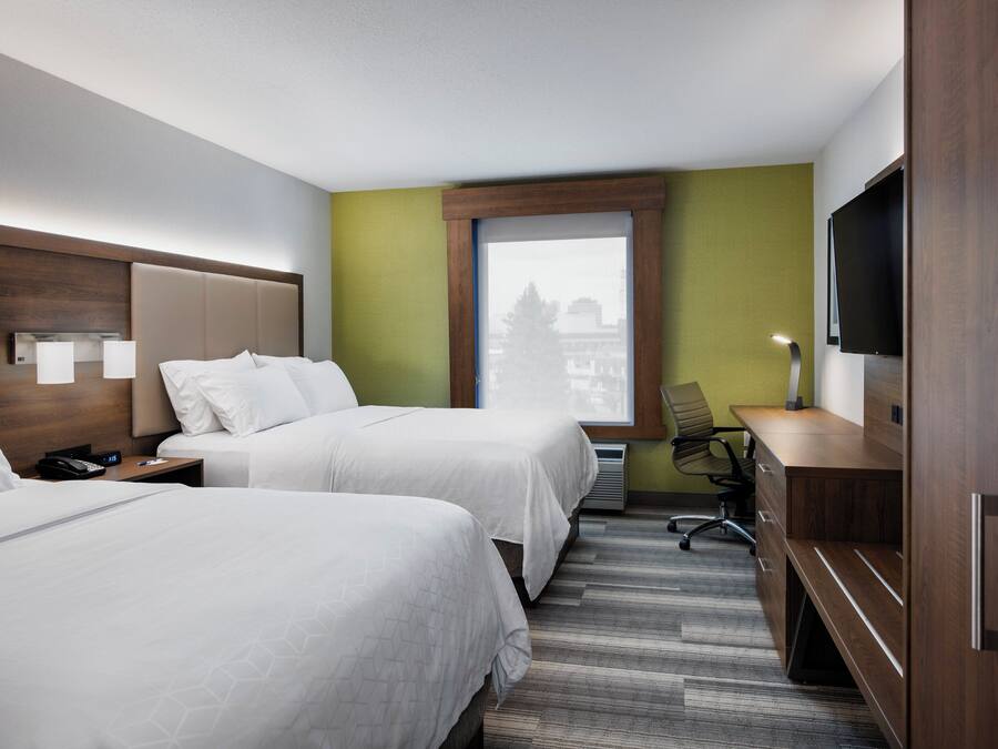 A hotel room with two beds, a desk, a chair, a TV, and a window with a view.