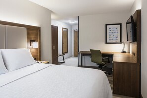 Quarto de hotel com cama, escrivaninha, cadeira e televisão sobre um móvel.