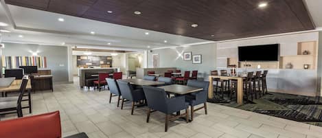 Un moderno vestíbulo de hotel con comedor, cocina y pantalla de televisión.