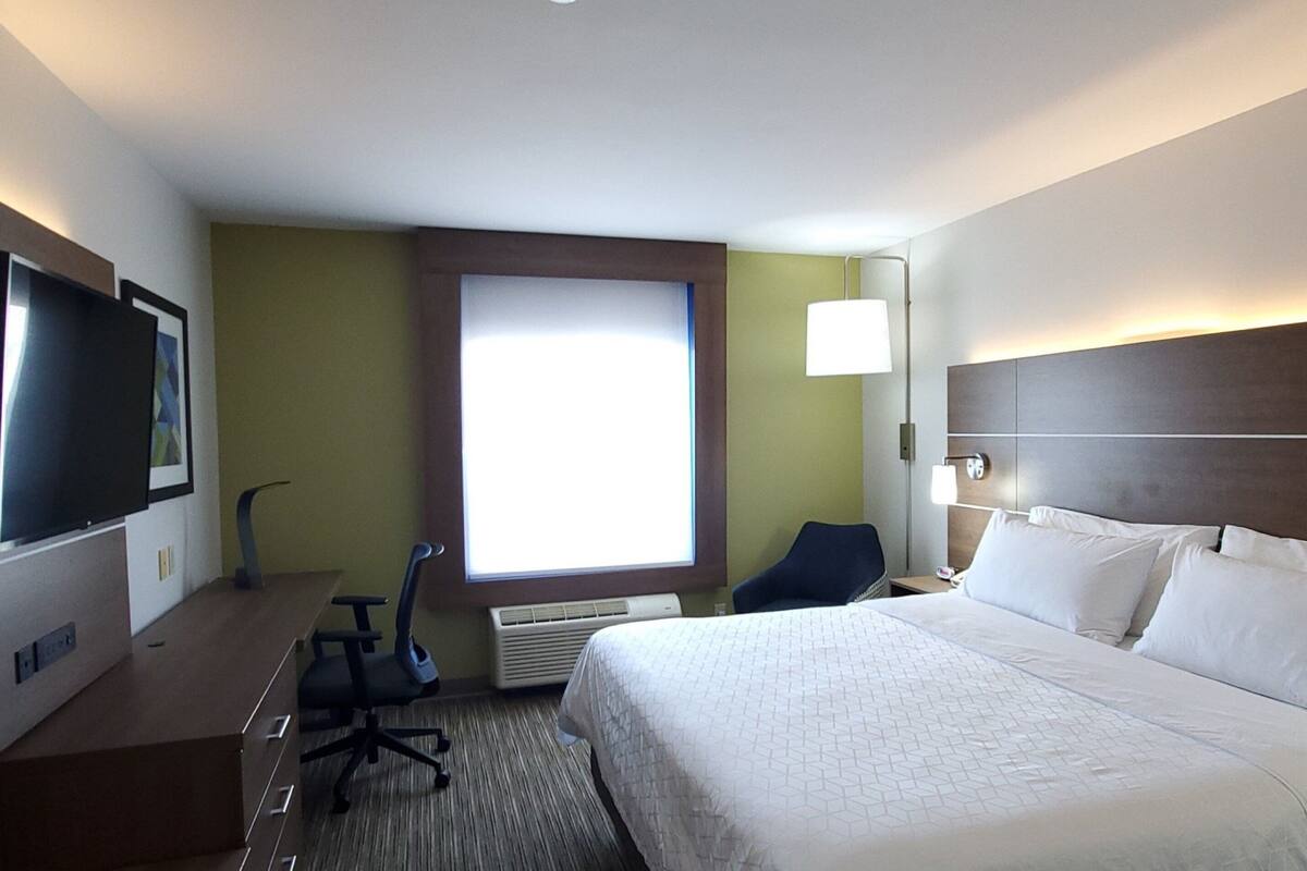 A hotel room with a large bed, a desk with a chair, a television, and a window with blinds.