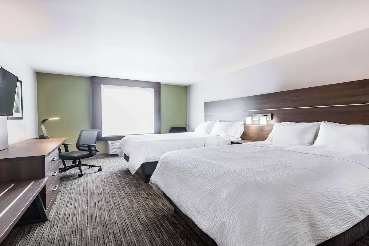 A hotel room with two beds, a desk, a chair, and a large window.