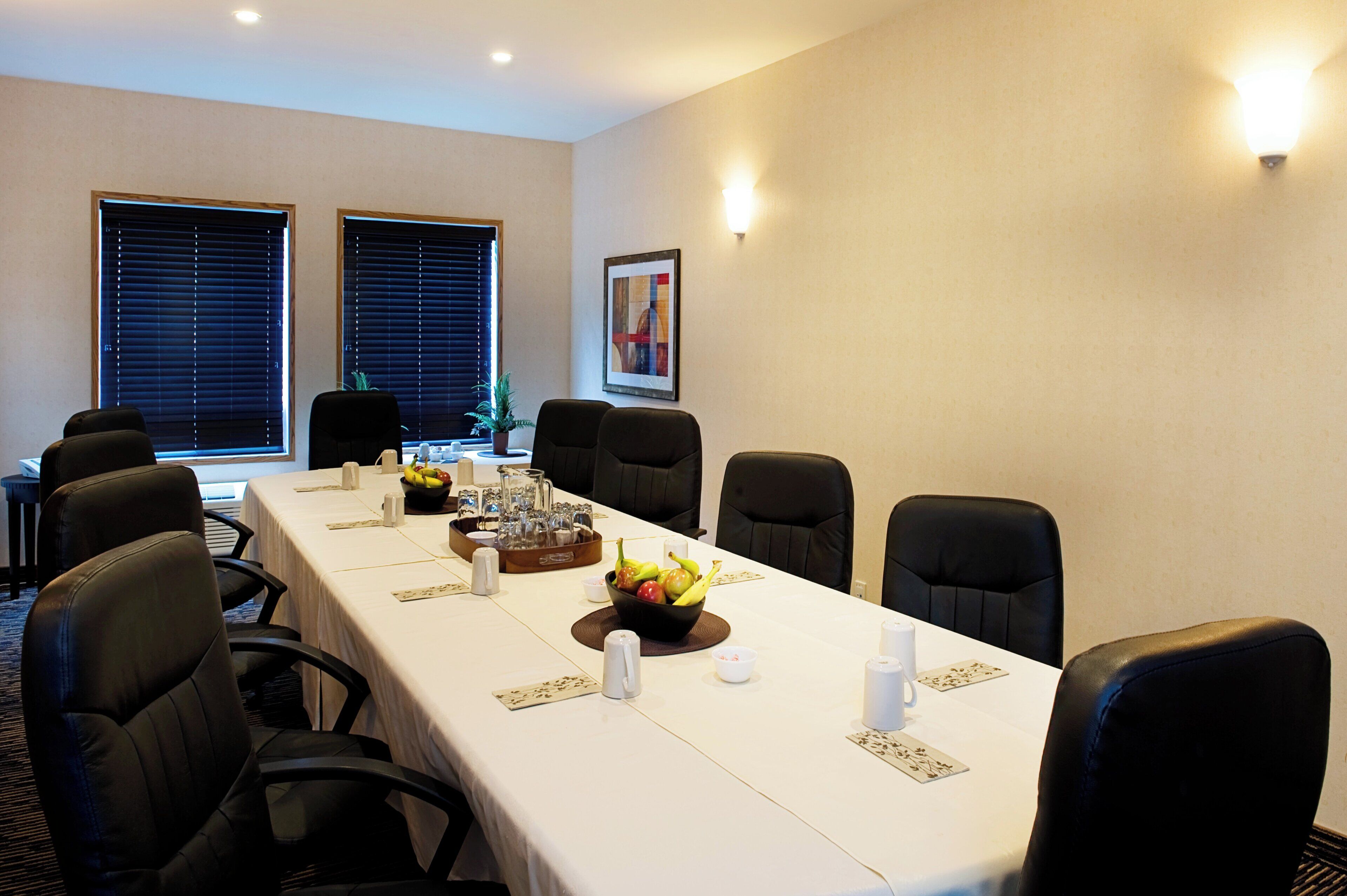 A conference room with a long table, chairs, a fruit bowl, and a painting on the wall.