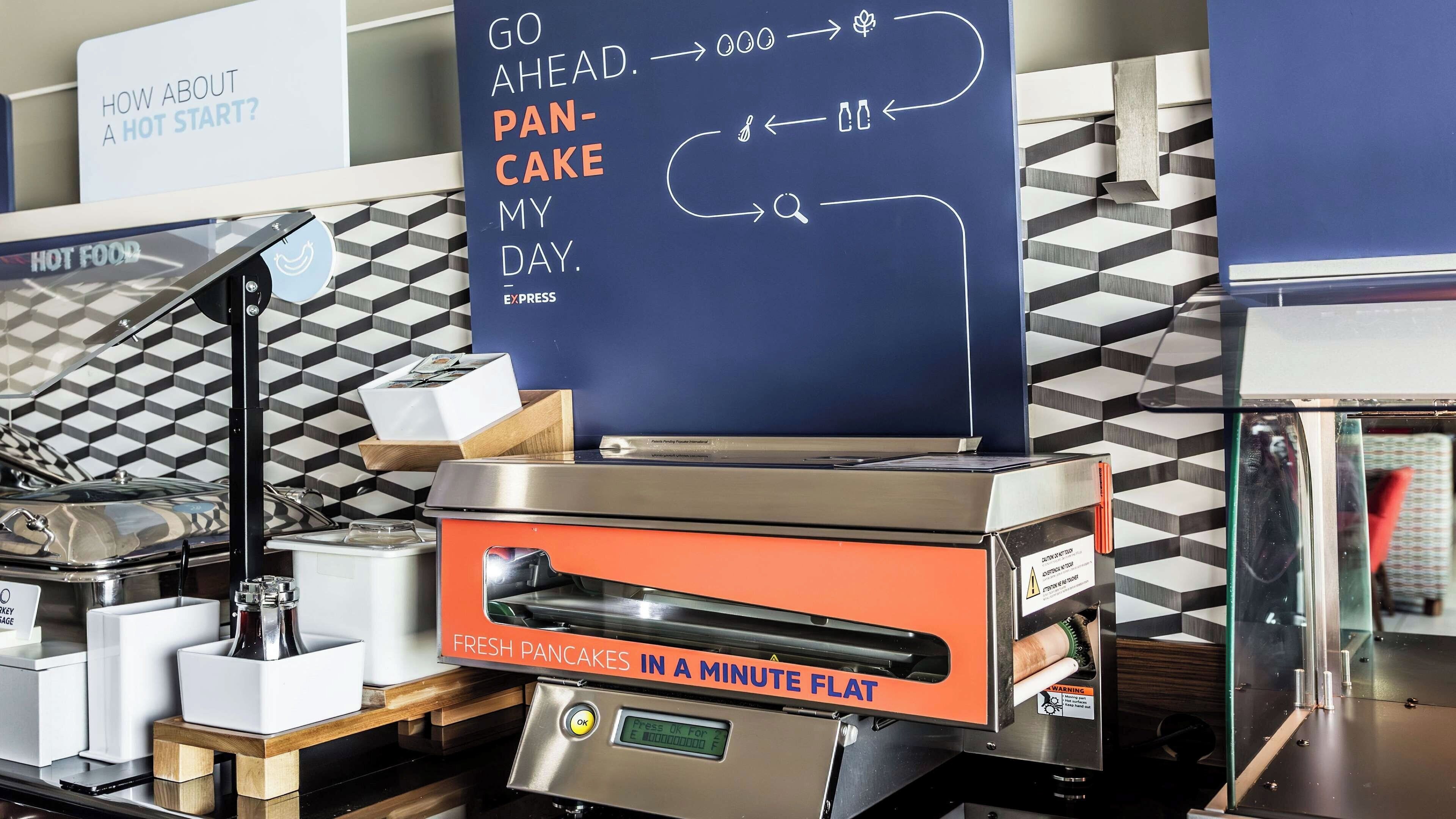 Una zona de cocina con un panel de menú digital que muestra opciones como 'GO AHEAD. PANCAKE MY DAY' y 'PANQUEQUES FRESCOS EN UN MINUTO'.