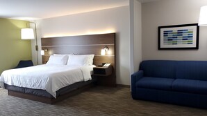 A hotel room with a bed, a nightstand, a blue sofa, a wall-mounted lamp, and a framed picture. - Holiday Inn Express & Suites Regina-South by IHG (Regina)
