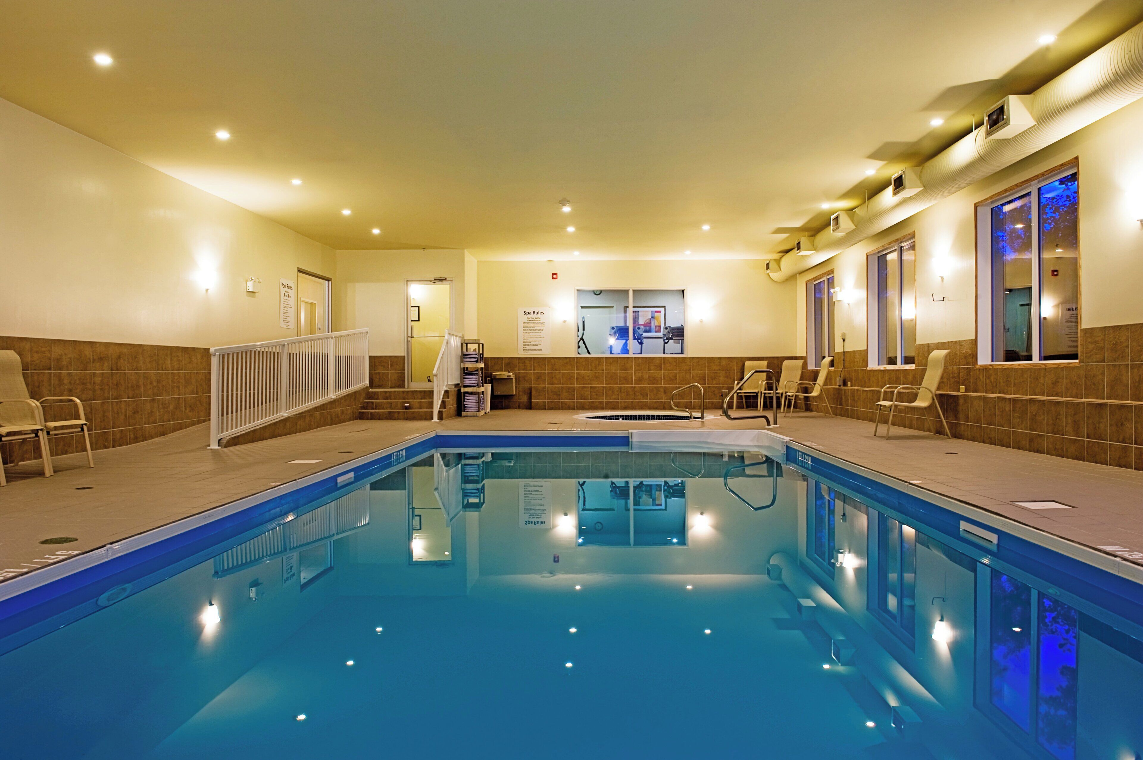 A hotel swimming pool with a tiled deck, lounge chairs, and a spa area.