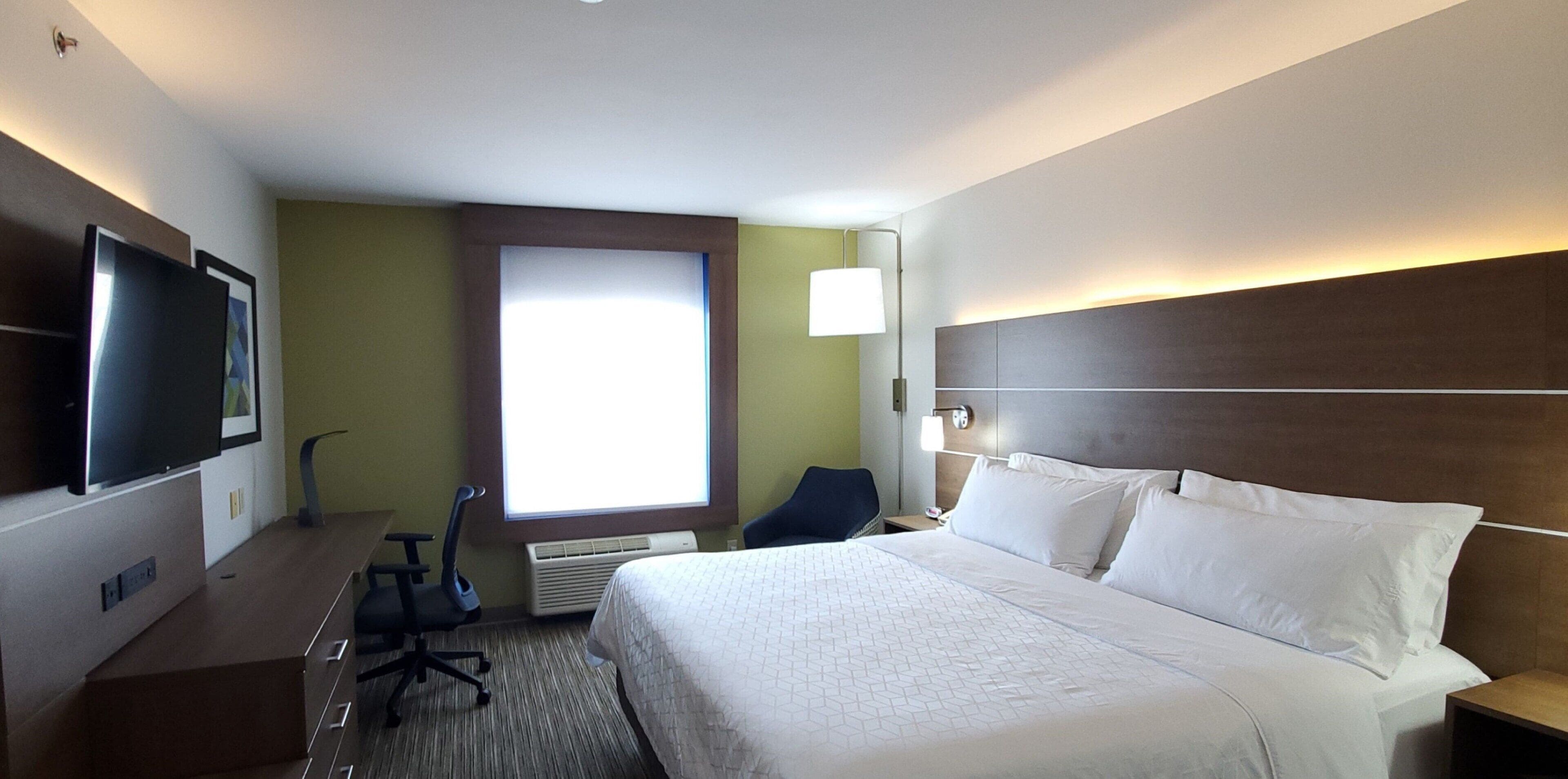 Une chambre d’hôtel avec un lit, un bureau, une chaise, une télévision et une fenêtre.