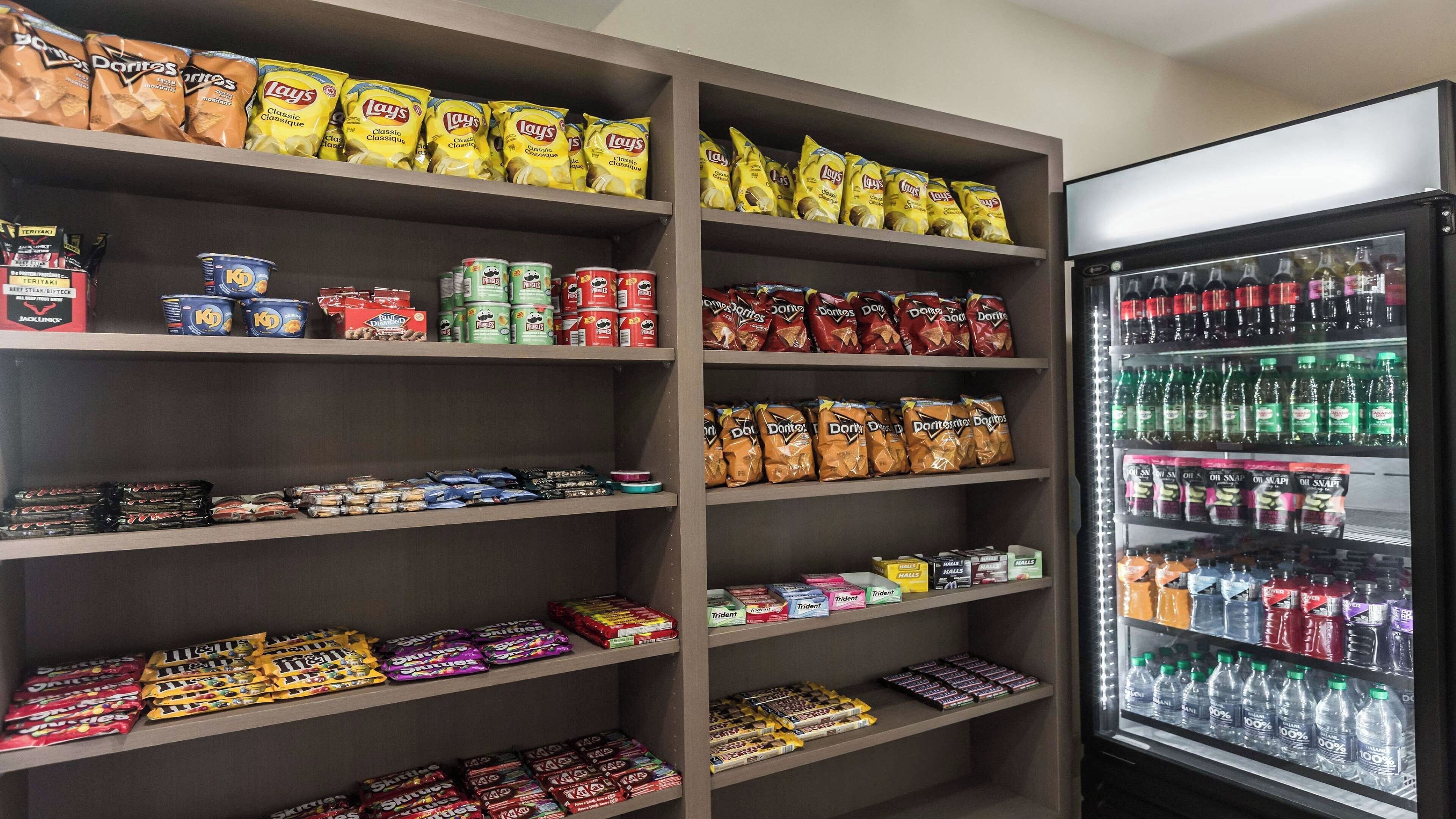 A snack and beverage display in a store, including bags of Lay's Classic and Doritos, canned drinks, and bottled water.
