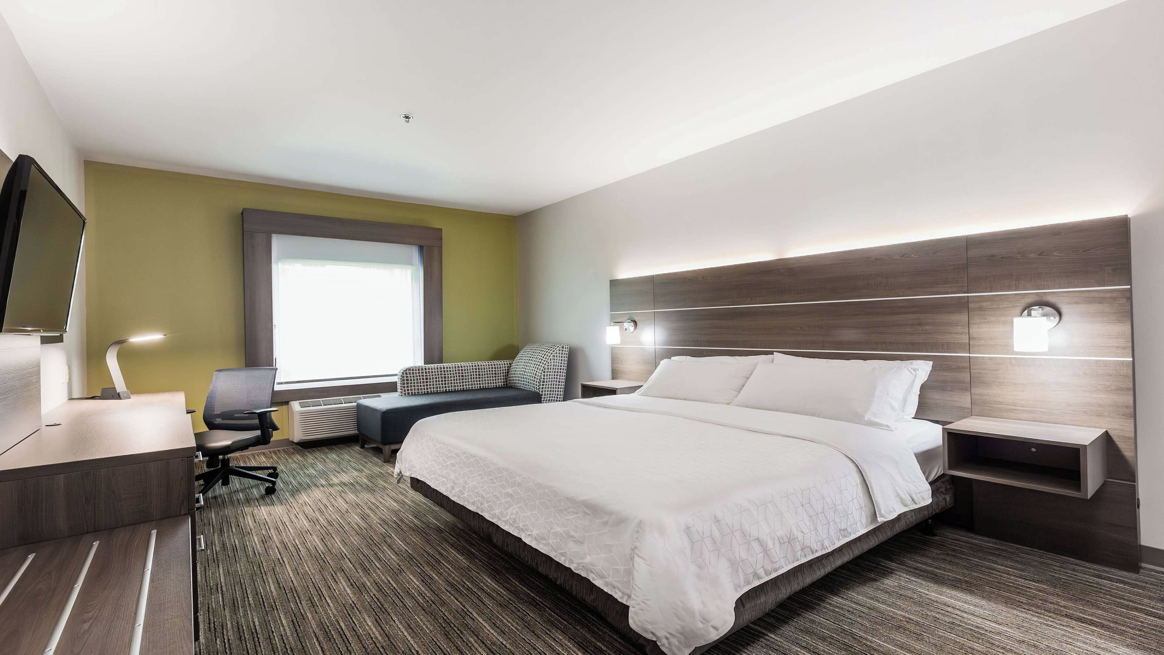 Une chambre d’hôtel moderne avec un grand lit, un bureau avec une chaise, une petite table et un téléviseur.