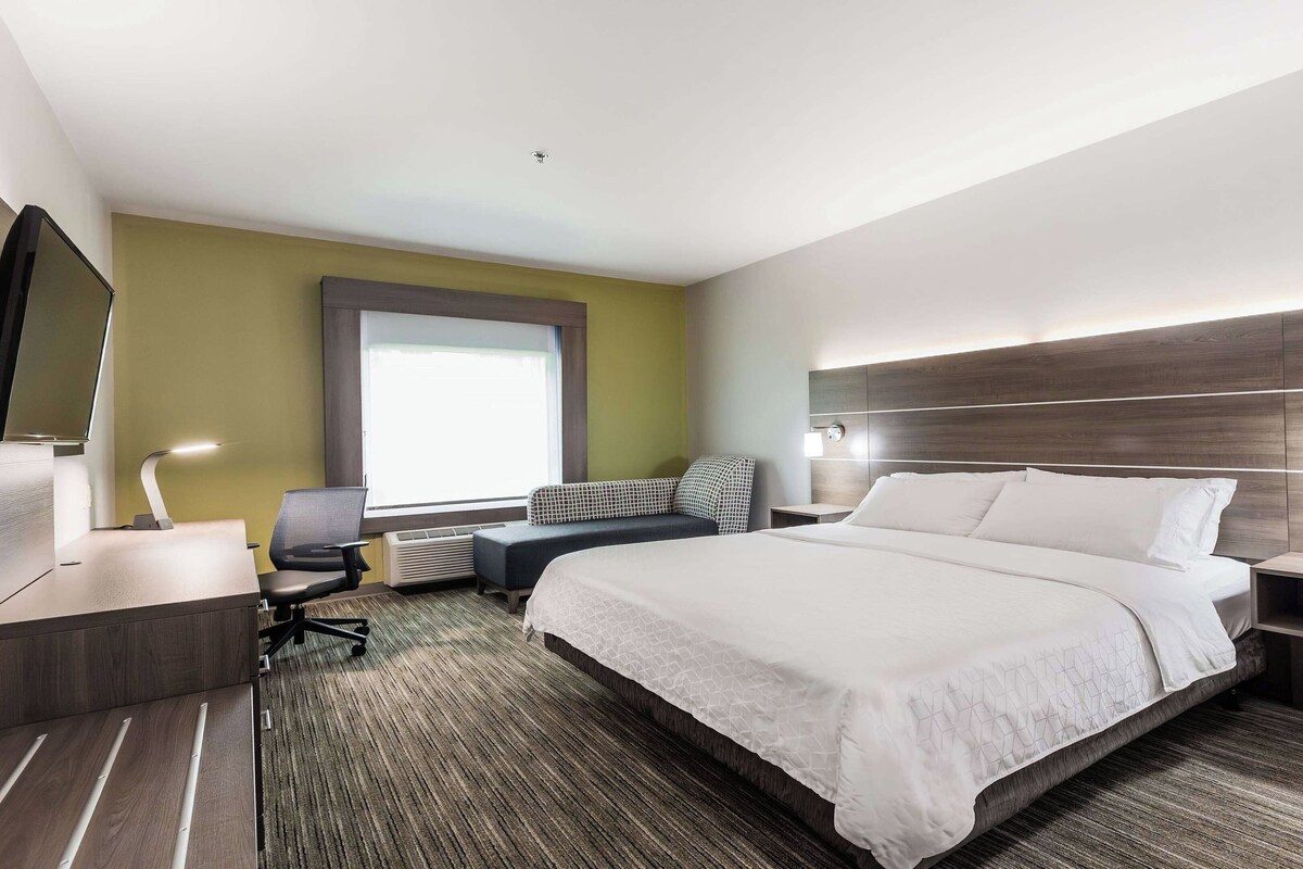 A modern hotel room with a large bed, a desk with a chair, a small table, and a TV.
