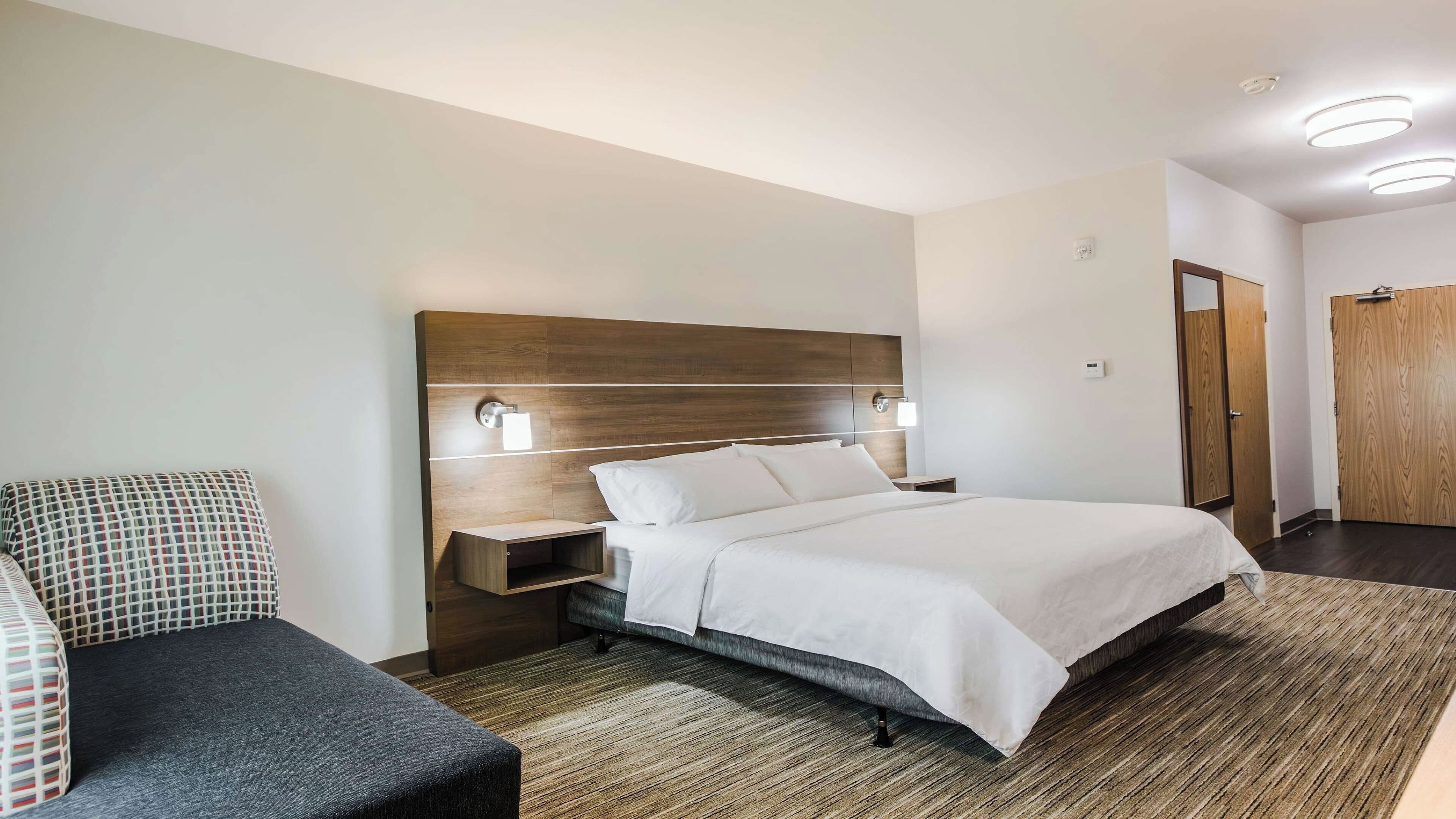 A modern hotel room with a large bed, bedside tables, a sofa, and a wooden wardrobe.