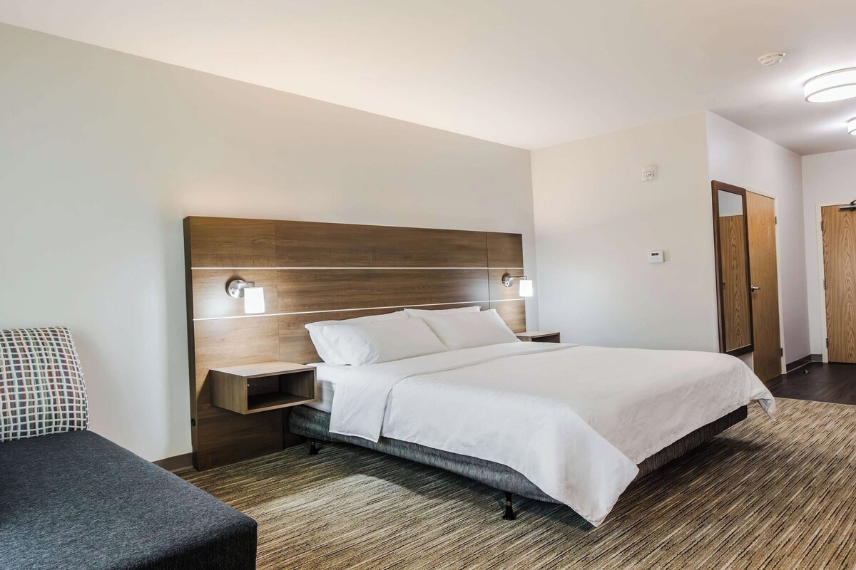 A modern hotel room with a large bed, bedside tables, a sofa, and a wooden wardrobe.