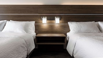 A hotel room with two beds, a wooden headboard, and a nightstand with two wall-mounted lights.
