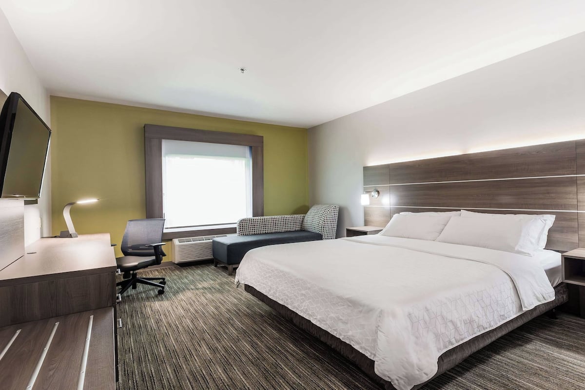 A modern hotel room with a large bed, a desk with a chair, a small table, and a TV.