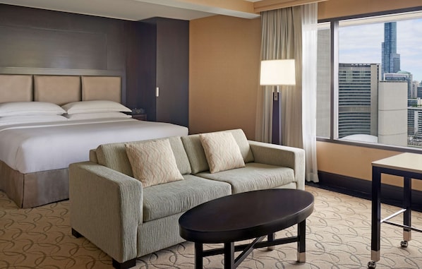 A hotel room with a large bed, a sofa, a small table, and a view of the cityscape. - Hilton Toronto (Toronto)