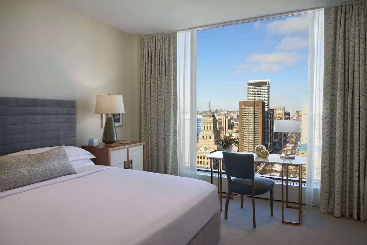 A hotel room with a bed, a desk, and a view of the cityscape.