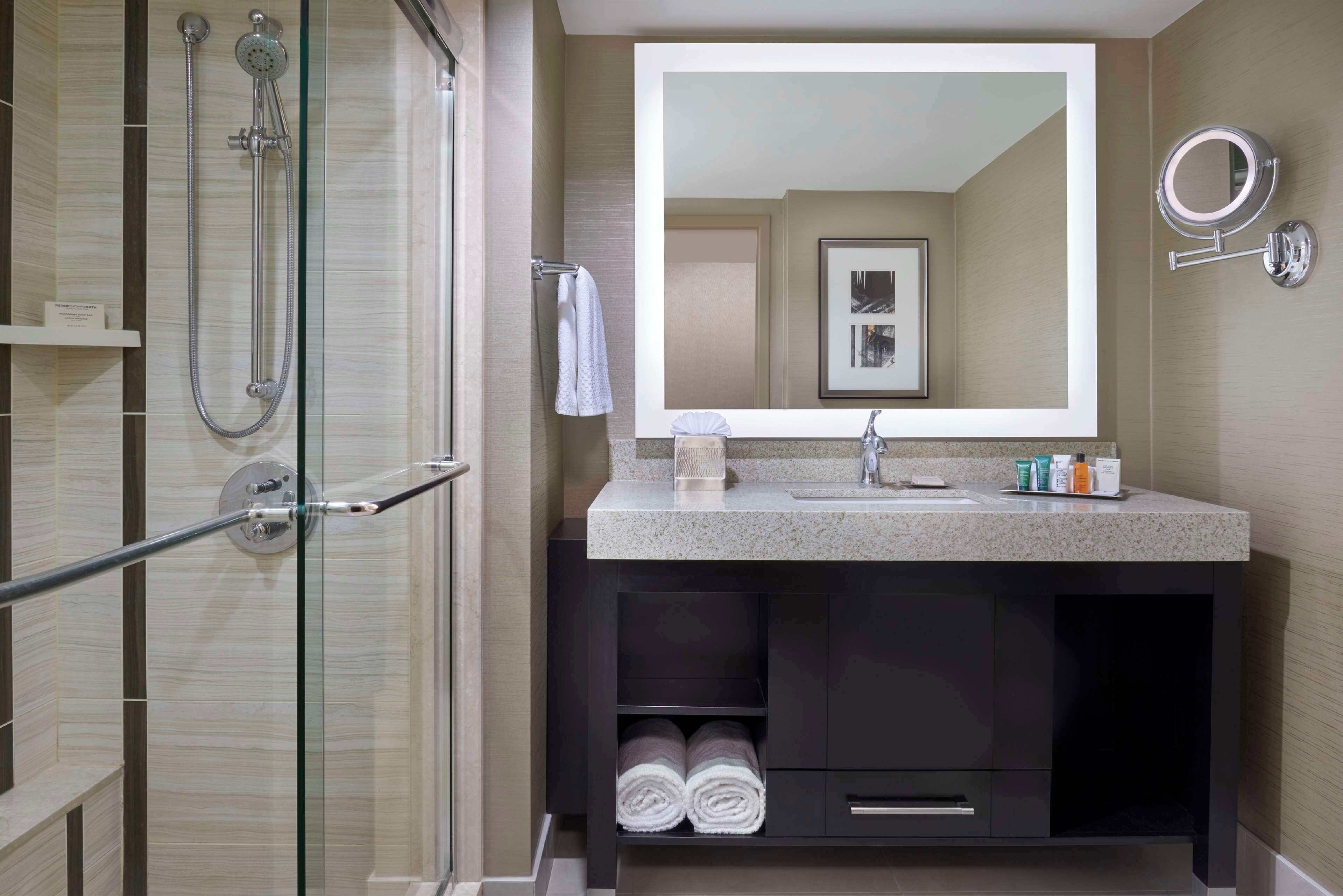A modern bathroom with a glass-enclosed shower, a large mirror, and a dark vanity with a countertop.