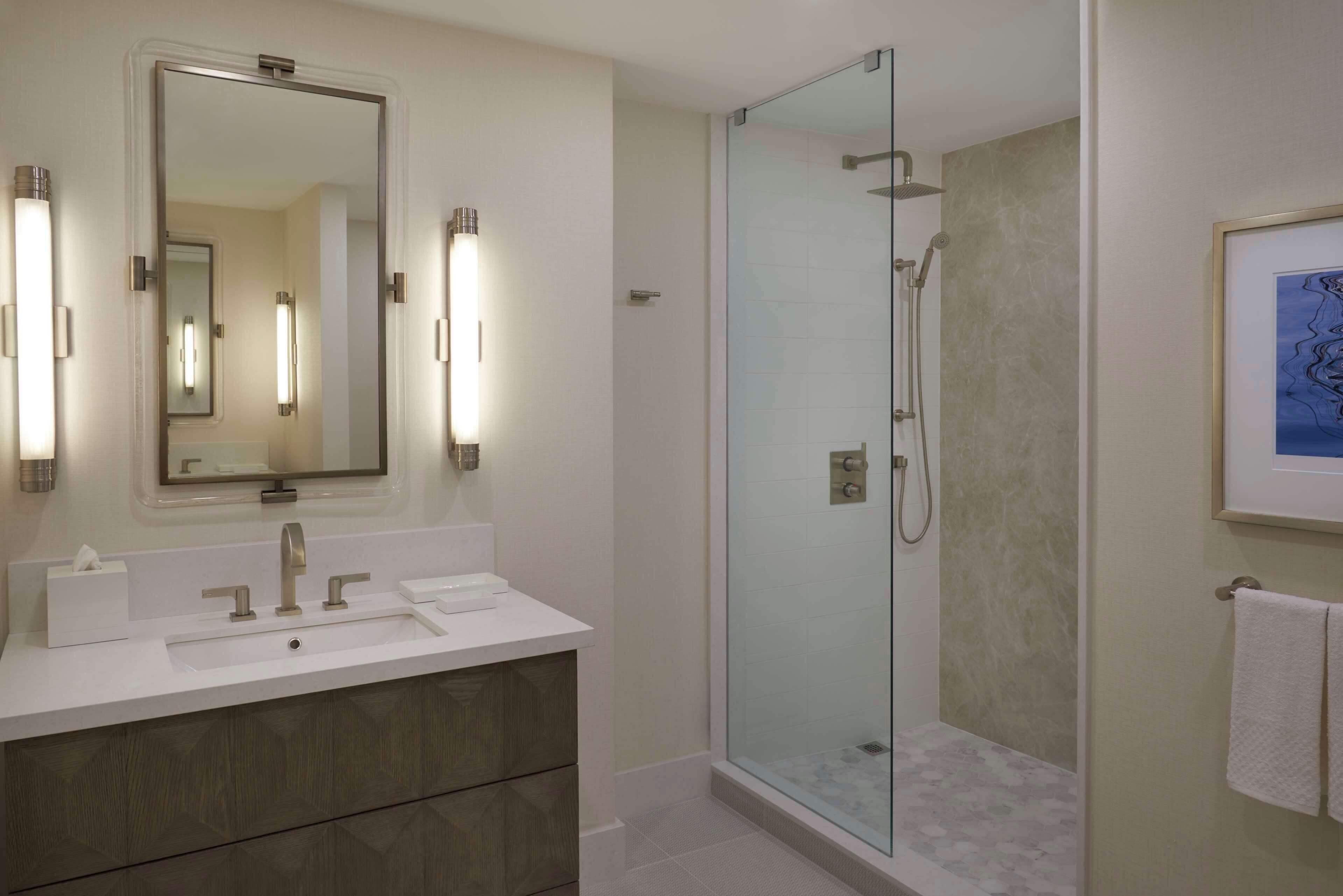 A modern bathroom with a glass-enclosed shower, a large mirror, and a white vanity with a towel rack.