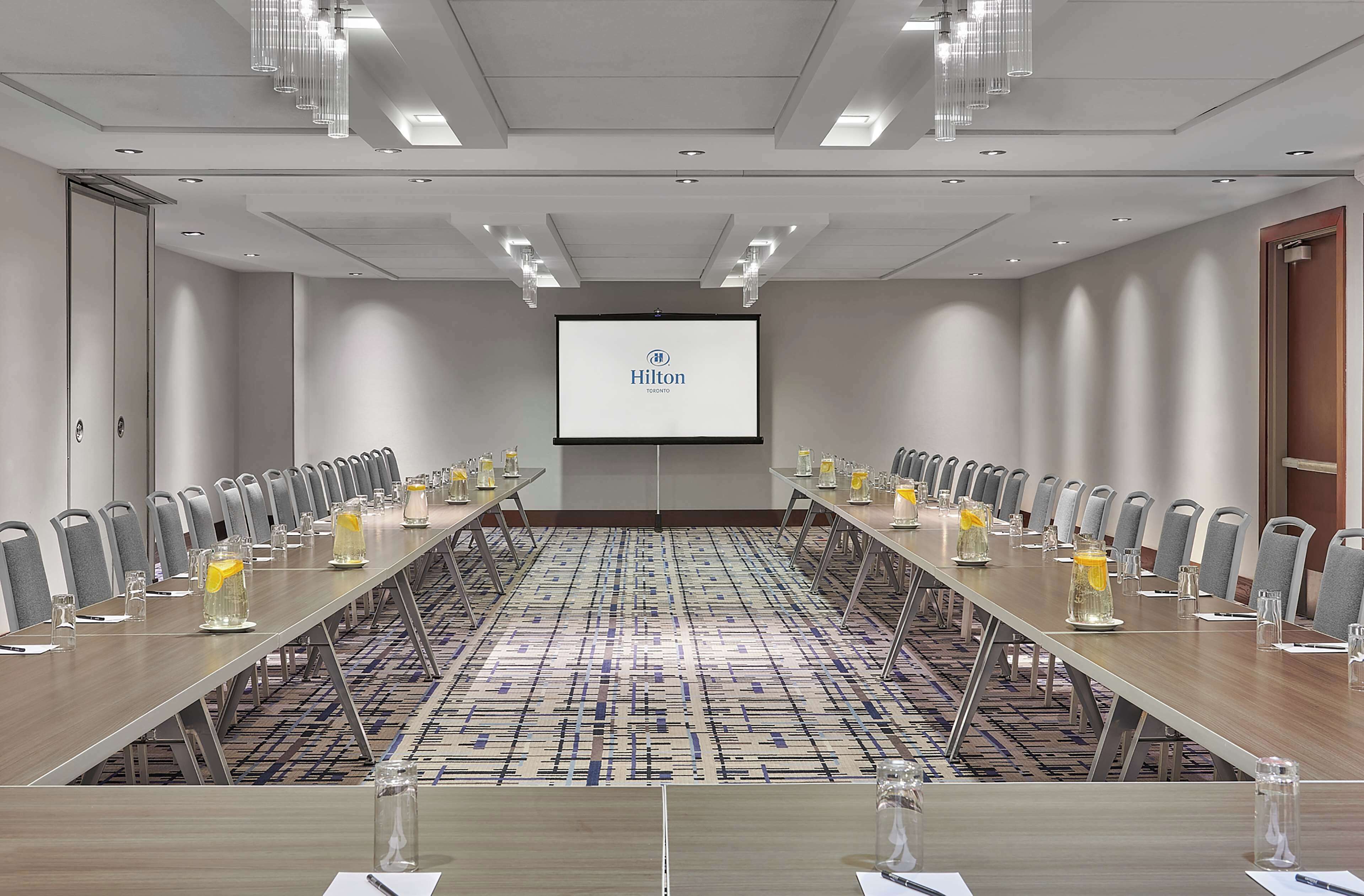 Un salón de conferencias con una larga mesa, sillas y una pantalla de proyector mostrando 'Hilton Toronto'.