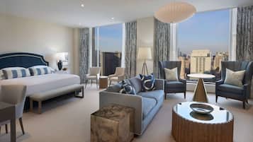 A modern hotel room with a large bed, a sofa, a coffee table, and a view of the city.