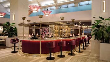 Een bar met een rode bar, meerdere krukken en decoratieve verlichtingsarmaturen.
