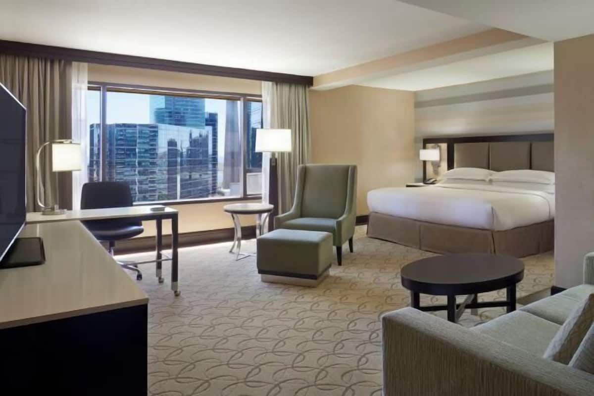 A hotel room with a bed, a desk, a chair, a small table, and a sofa.