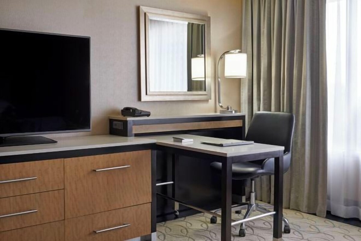 A hotel room with a desk, chair, television, and a mirror.