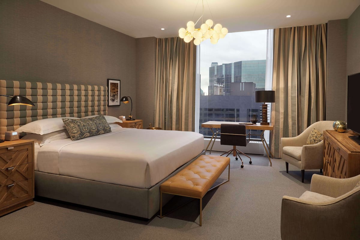 A modern hotel room with a large bed, a desk, a chair, and a view of the city.